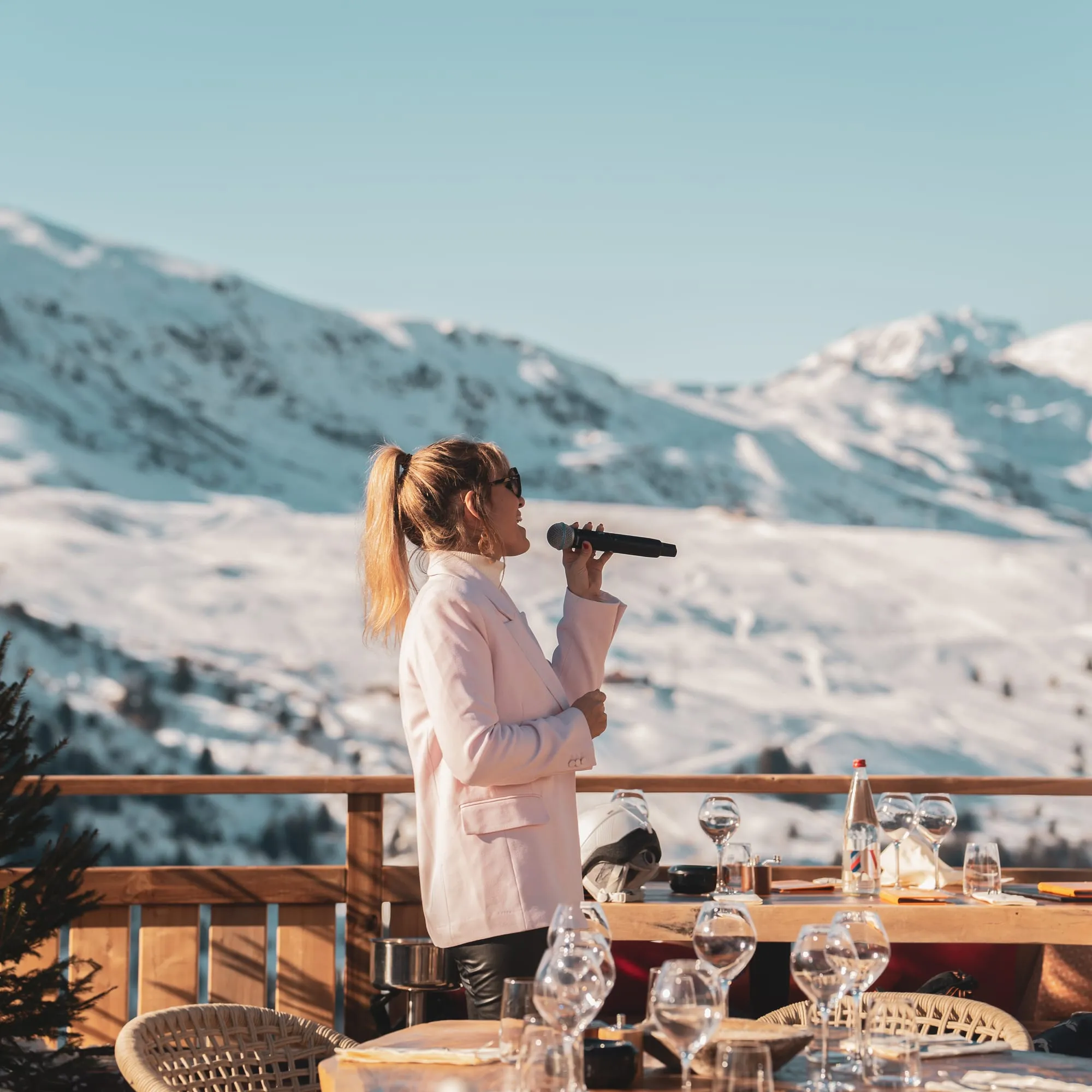 Une chanteuse au micro sur la terrasse, les sommets enneigés derrière elle.