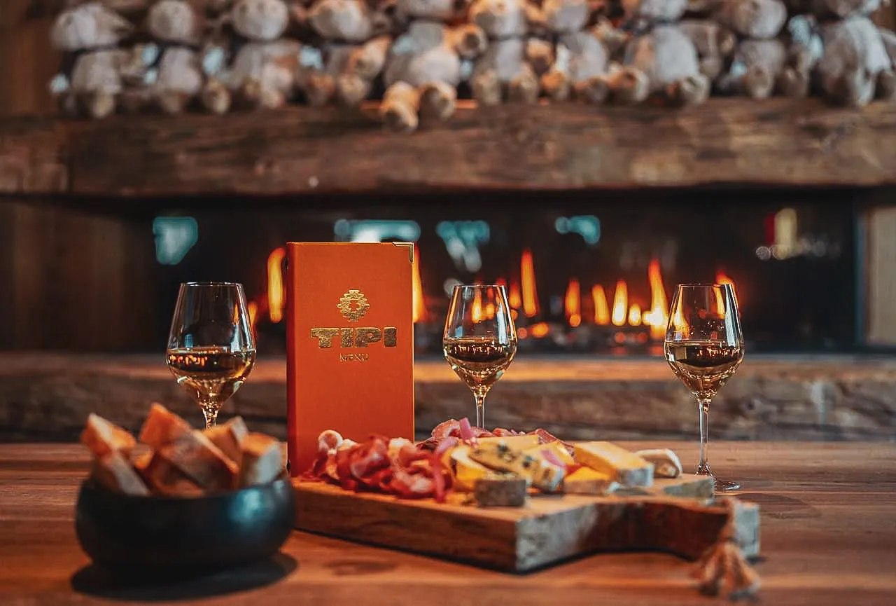 Devant la cheminée, une planche de charcuterie et de fromage, la carte de Tipi et des verres de vin.