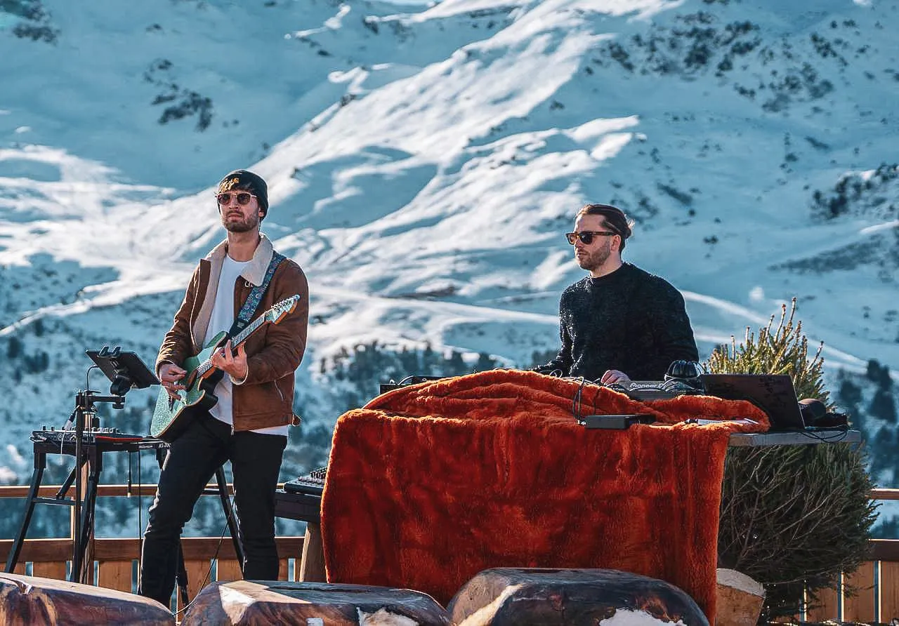 Un guitariste et un DJ jouent sur la terrasse, face aux pistes enneigées.