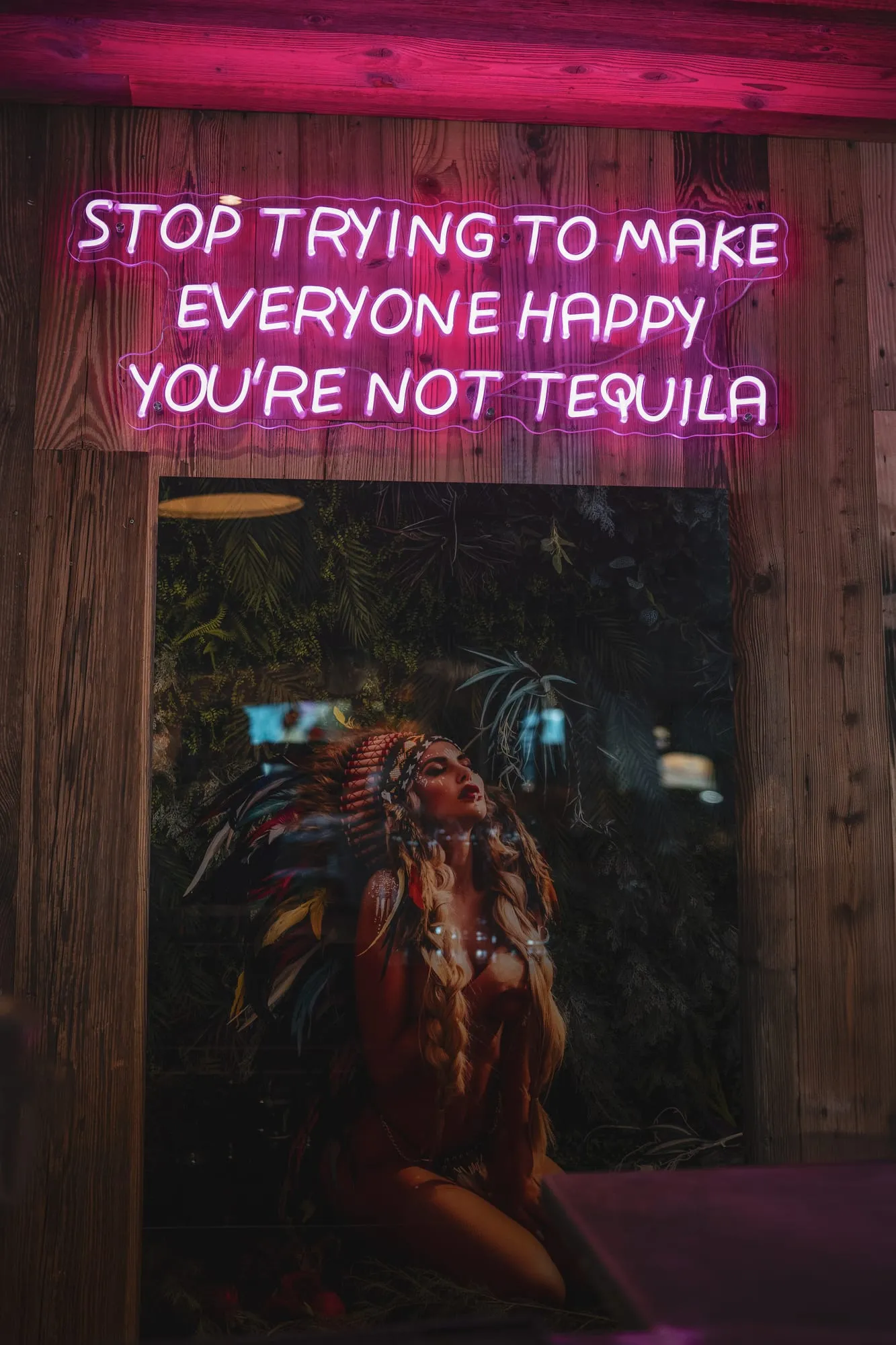 Le néon rose « Stop trying to make everyone happy, you’re not Tequila » au-dessus d’une porte en bois.