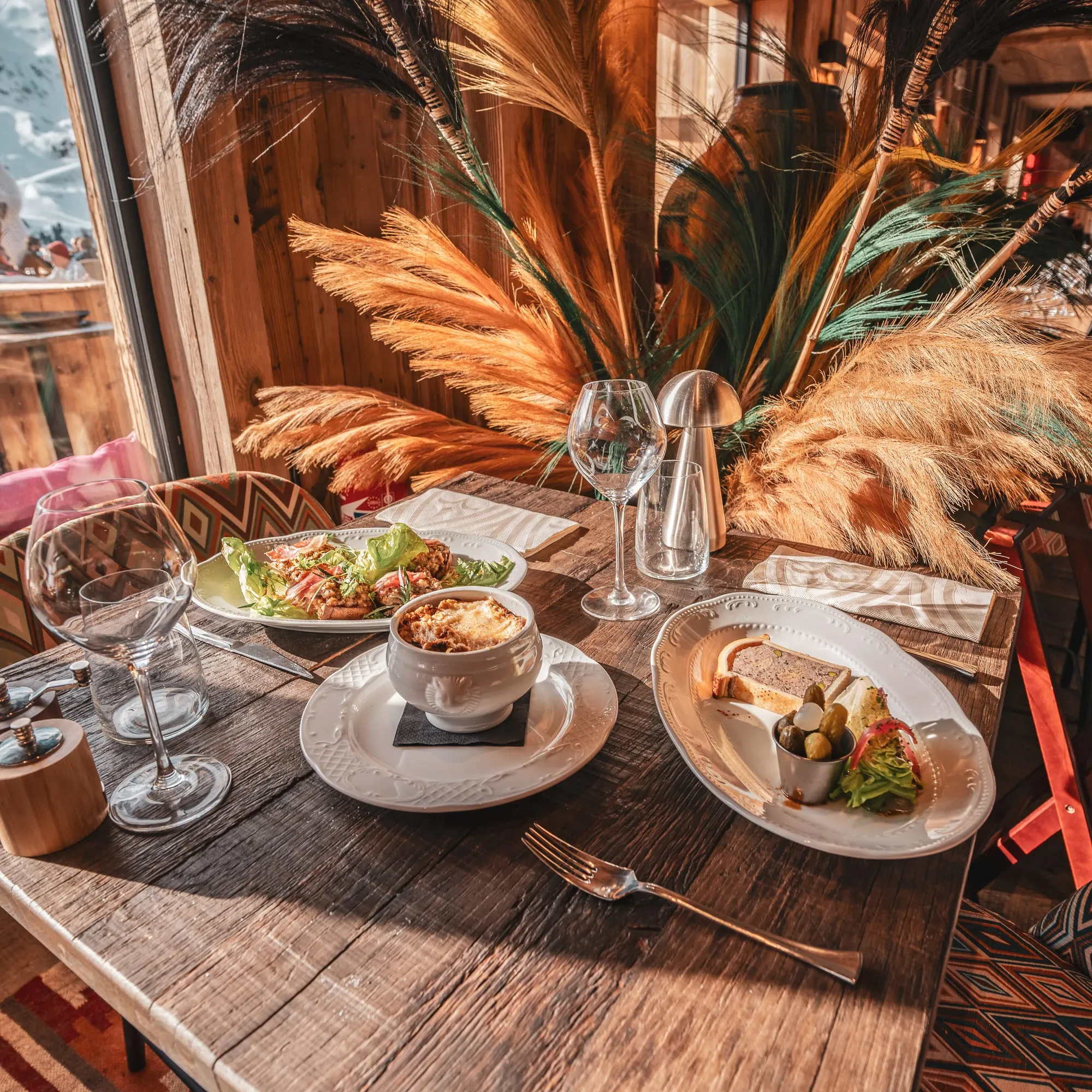Une table de Tipi dressée : assiettes, verres et bouquets de pampa, dans la lumière du chalet.
