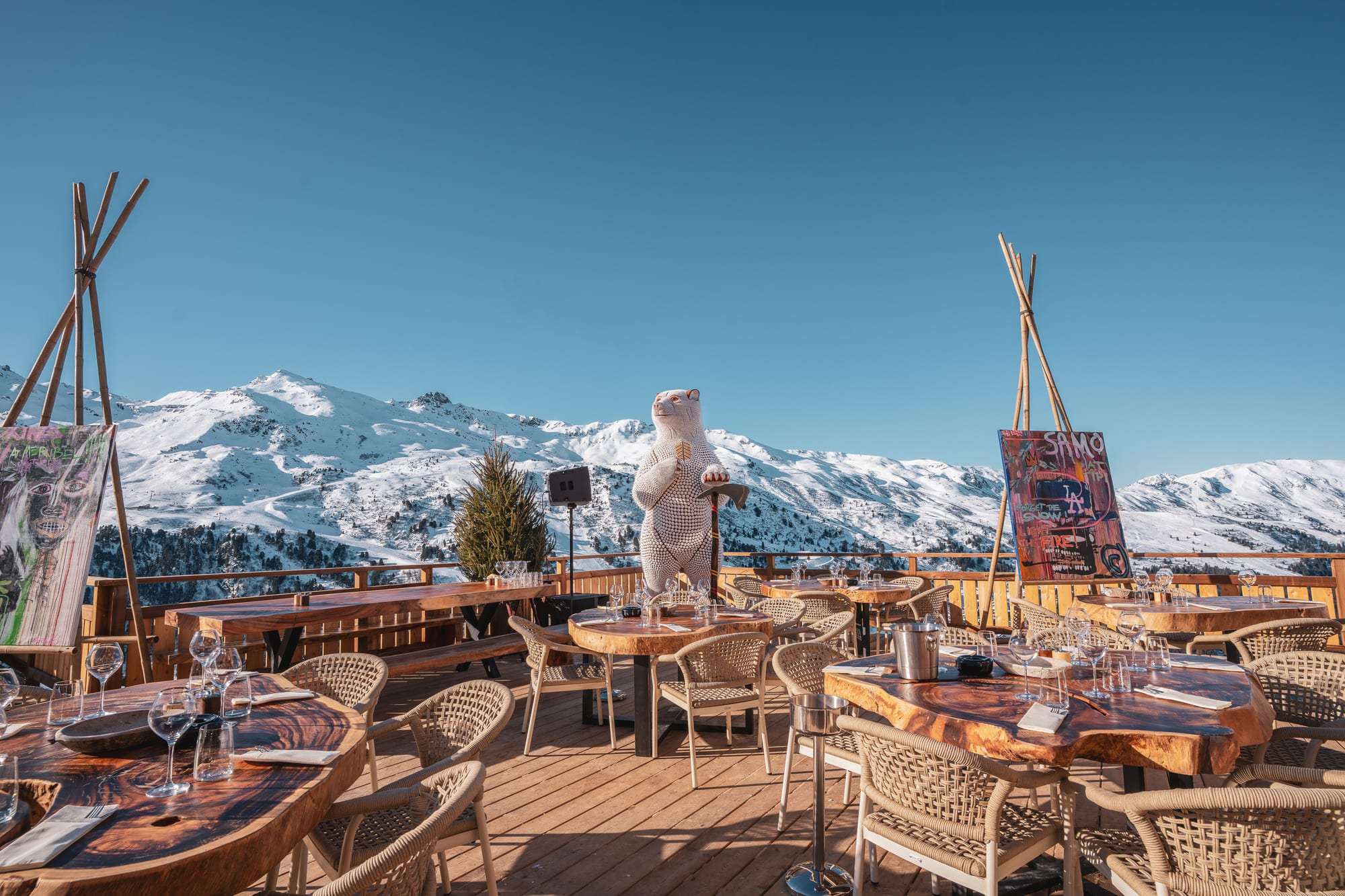 La terrasse de Tipi face aux sommets enneigés : les tipis, l’ours géant et les tables au soleil.